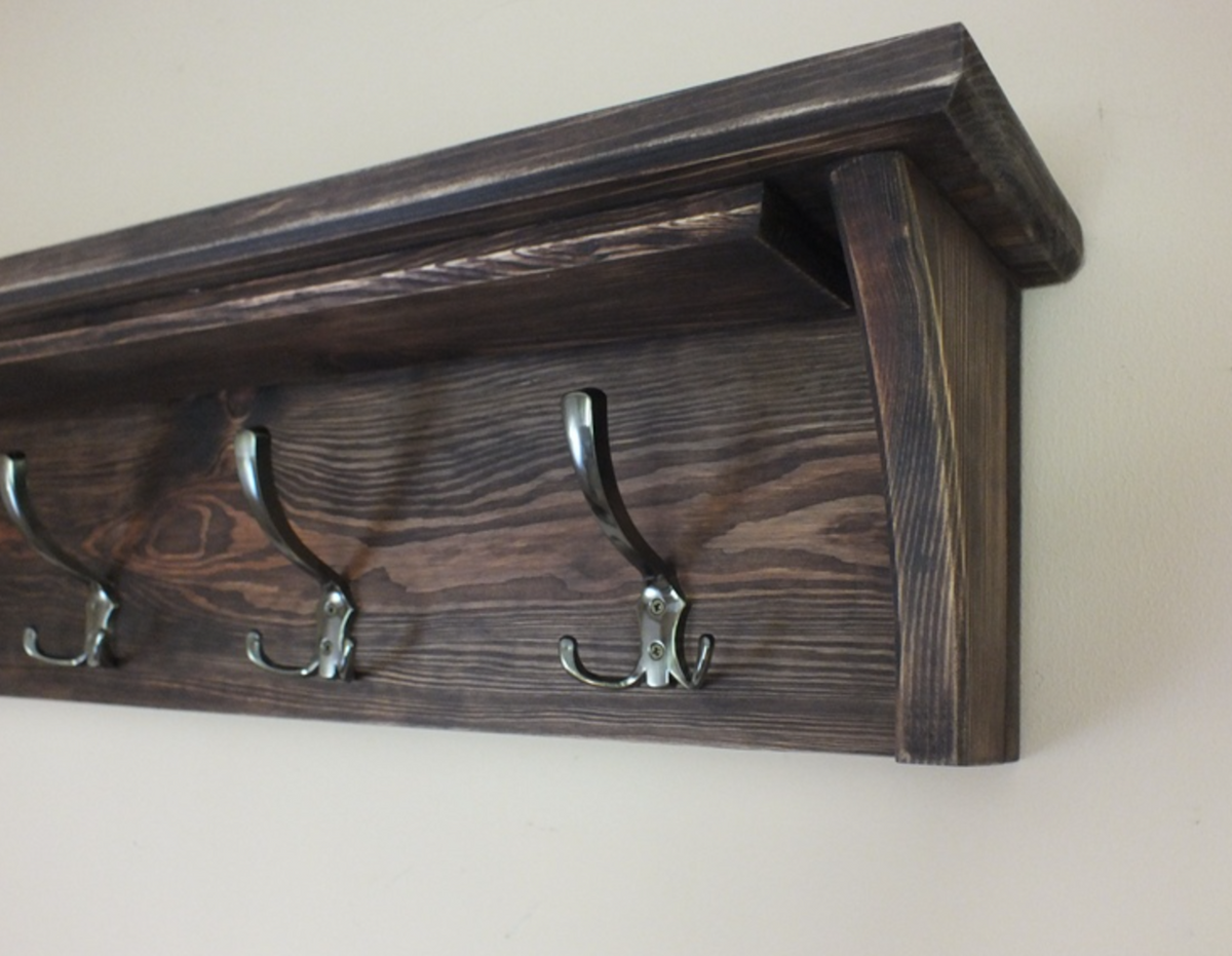 A dark brown wooden wall-mounted shelf with four metal coat hooks, shown against a plain off-white wall.