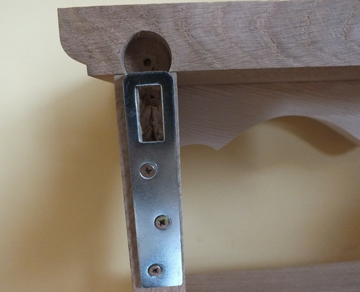 Close-up of a metal shelf bracket attached to a wooden shelf frame, with a screw and wood insert visible, against a pale yellow background.