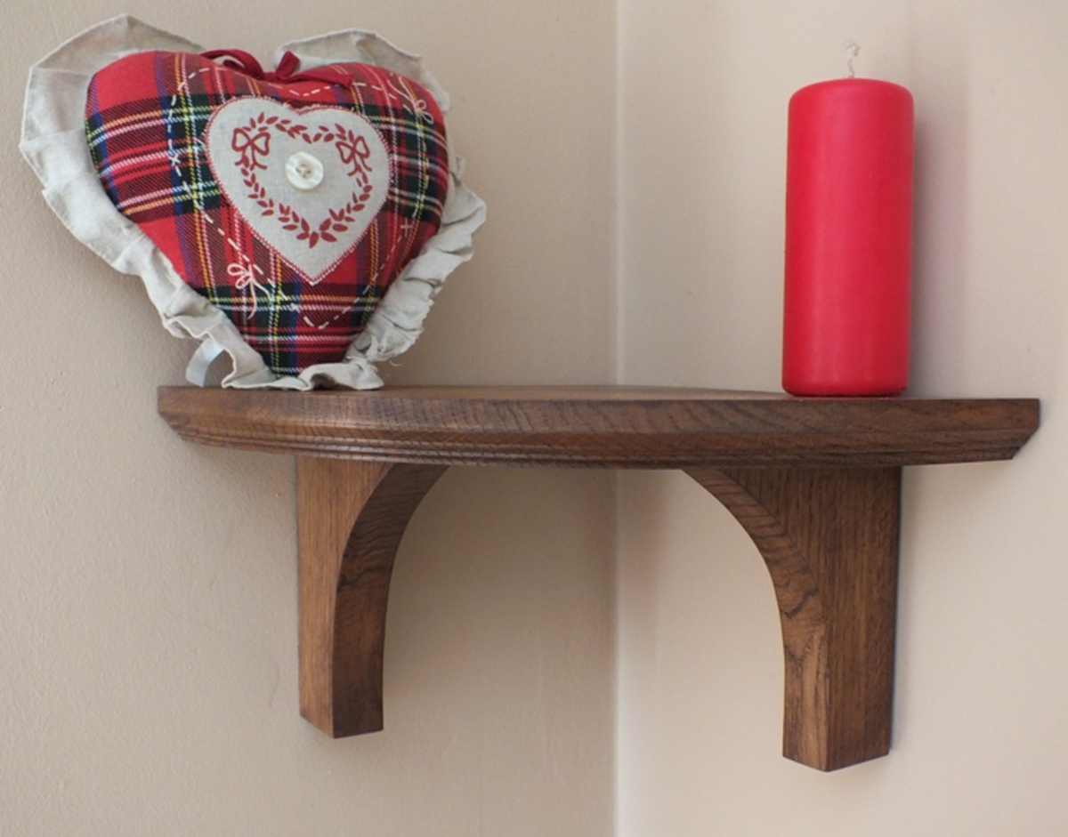 A dark brown wooden shelf mounted on a beige wall, styled with a red and green tartan heart-shaped pillow and a red pillar candle.