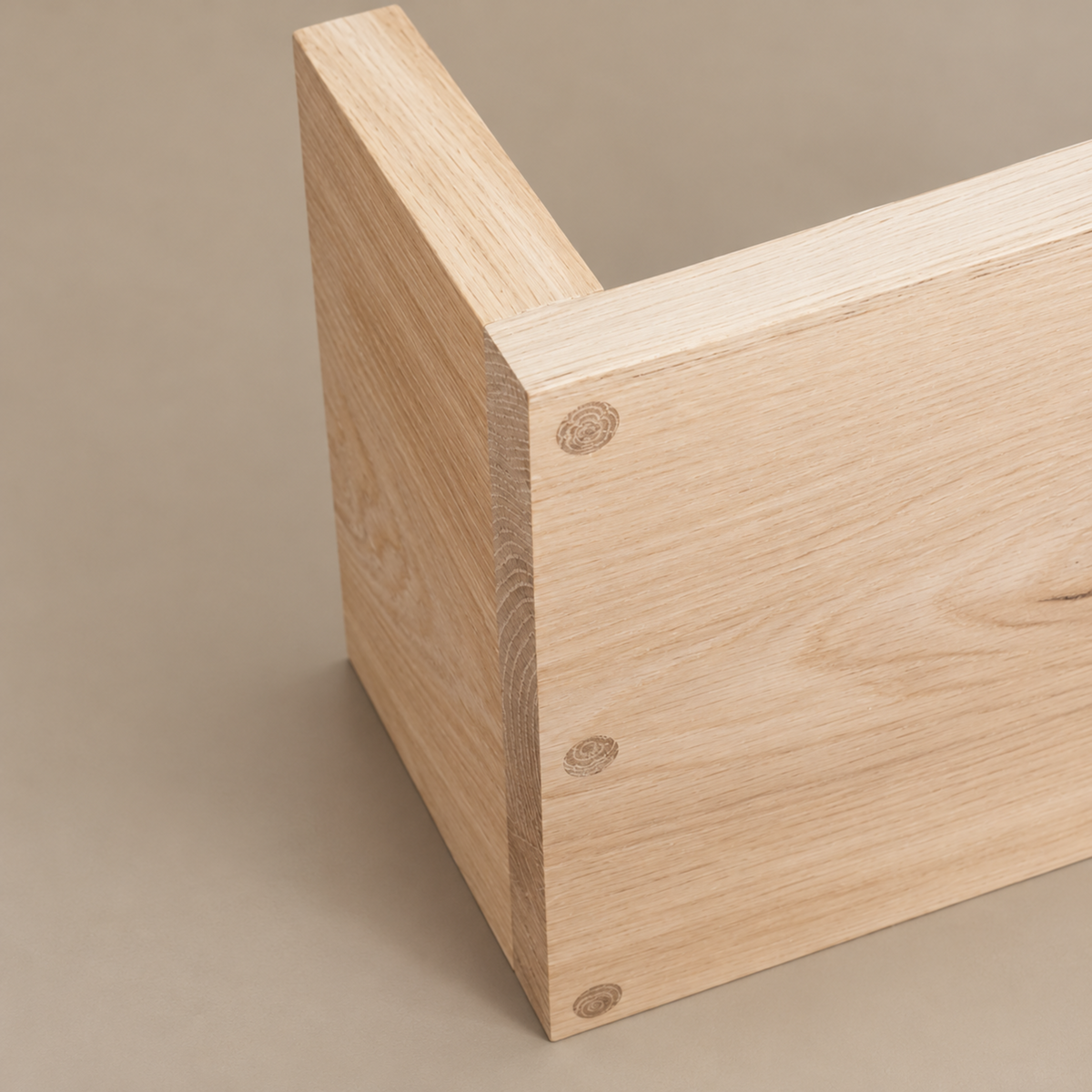 Close-up of a light natural wood furniture corner with visible grain and three round dowel ends, photographed on a plain warm beige background.