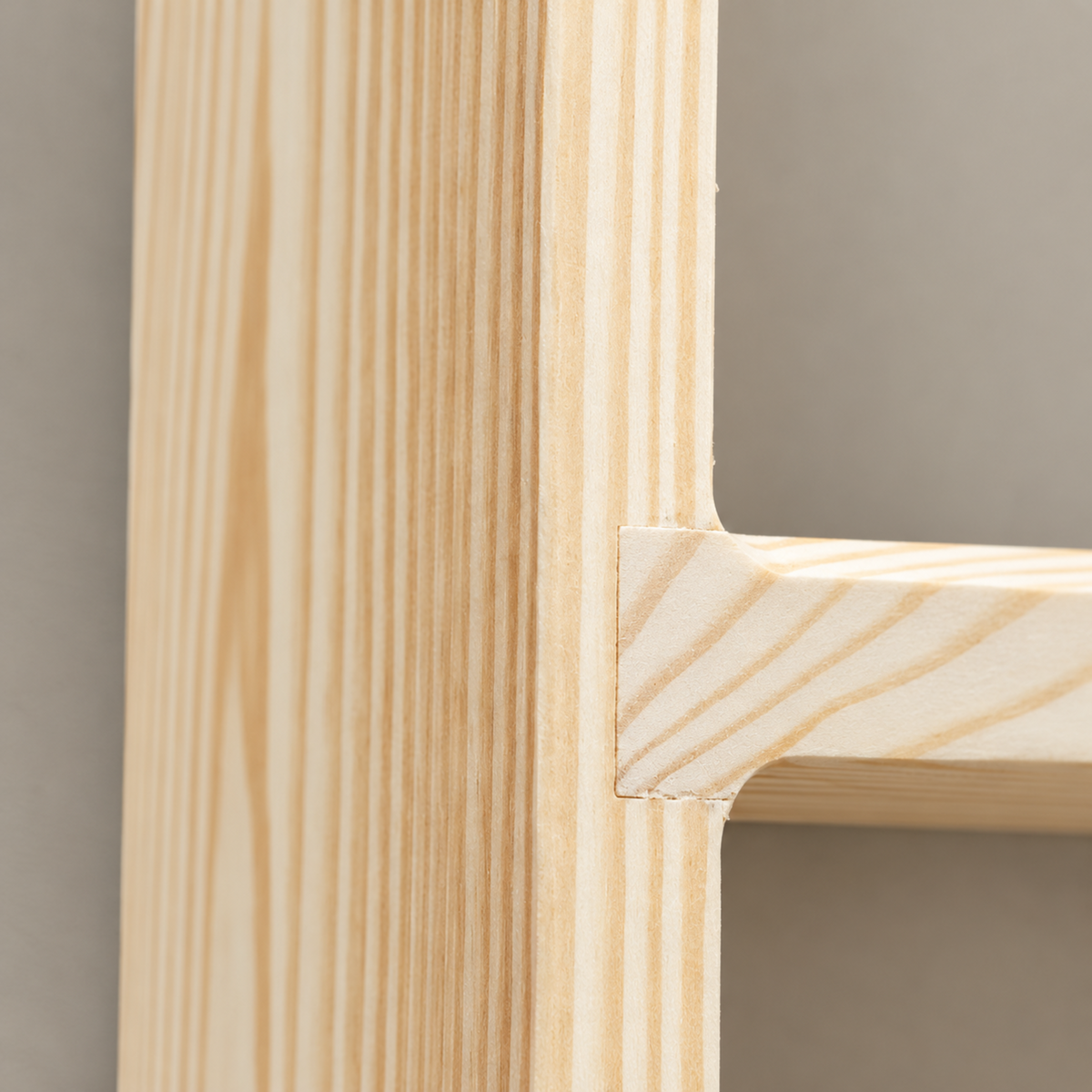 Close-up detail of a light natural wood shelf or cabinet corner with a mortise and tenon joint, showing the wood grain against a neutral gray background.