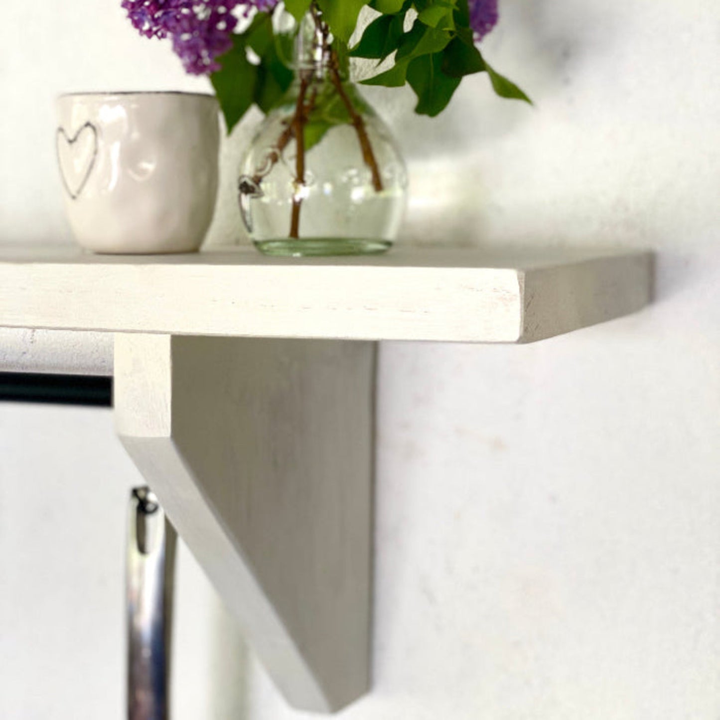 White wall-mounted shelf with a clear vase of purple flowers and a white mug.