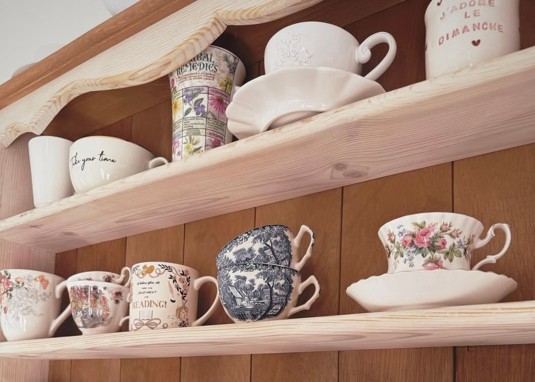 Wooden shelves with various ceramic mugs and teacups on a wooden wall background