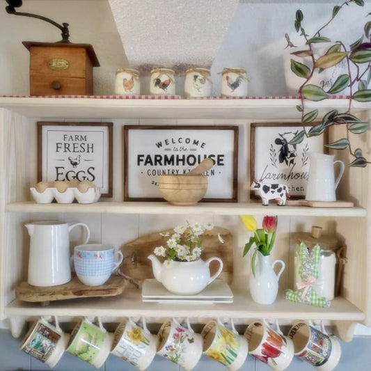 A cream-colored wooden wall shelf with hooks, mounted on a wall, displaying various kitchen decor items like mugs and a coffee maker.