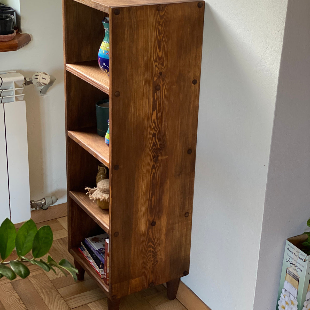 A rustic four-tier wooden bookcase with a warm medium-brown finish and visible wood grain, styled with decorative items on its shelves in a home interior setting.