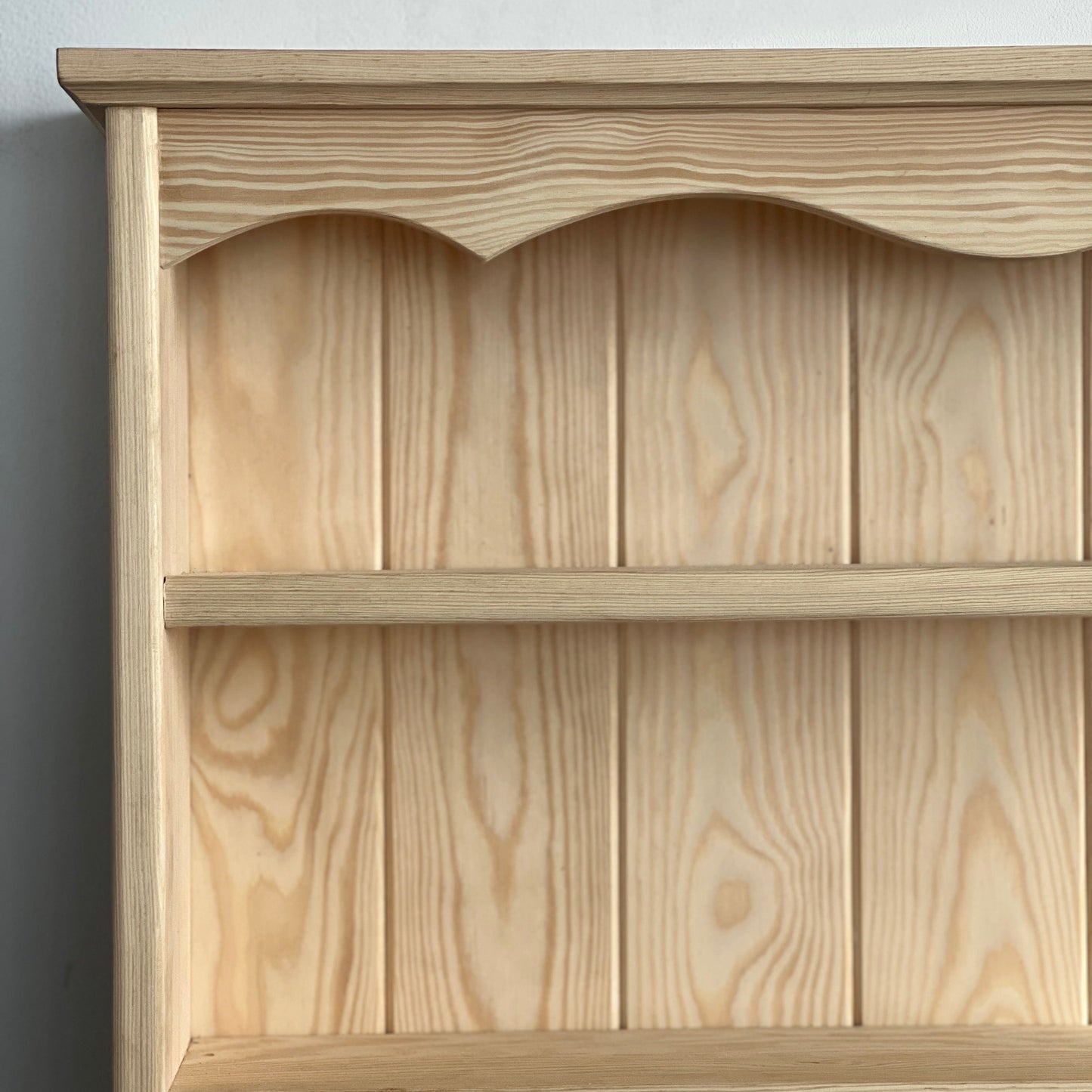 Wooden bookshelf with a scalloped edge design against a plain background