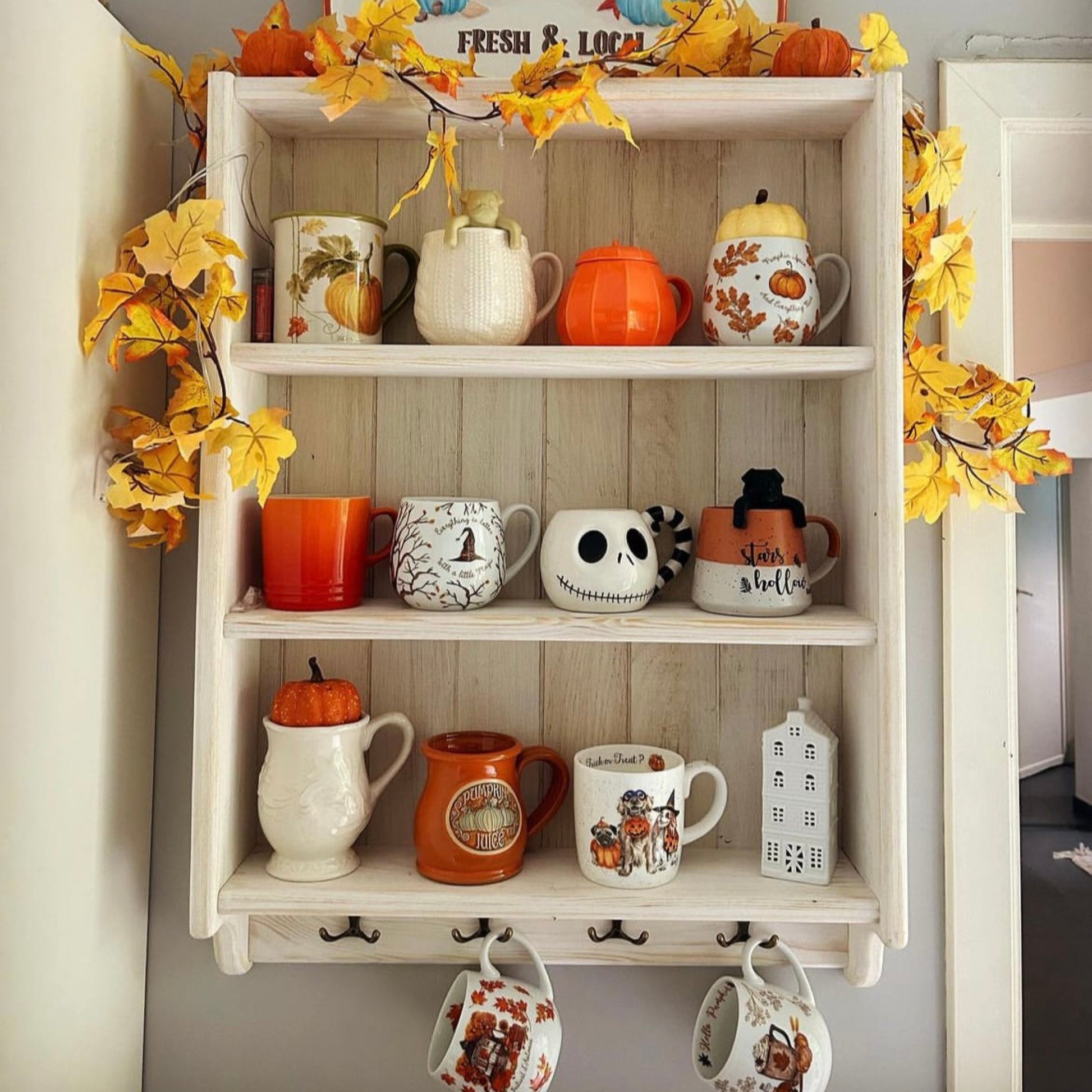 Shelf with Halloween-themed mugs and decorations, including a sign with a truck and pumpkins.