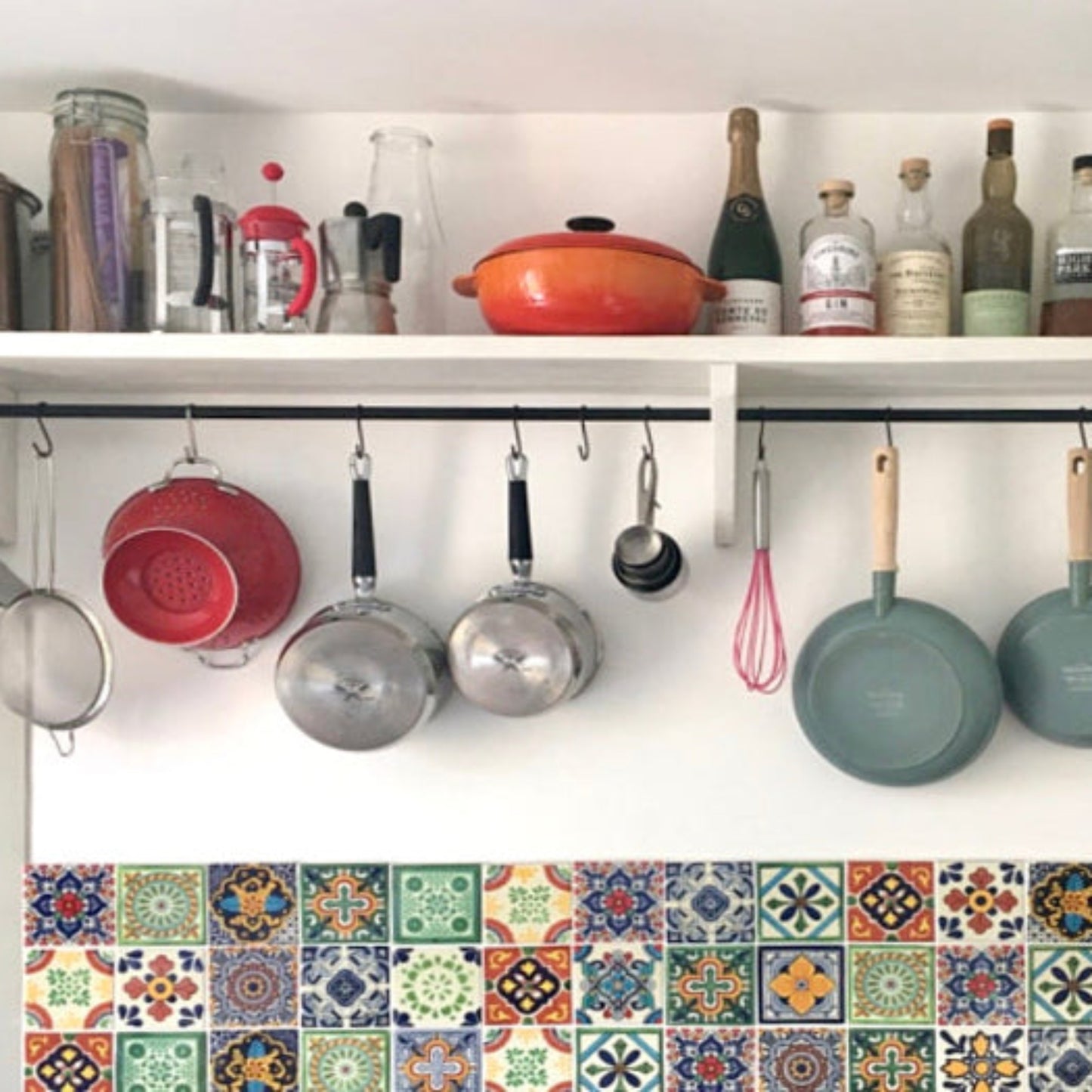 Kitchen shelves with pots, pans, and bottles above a colorful tiled backsplash.