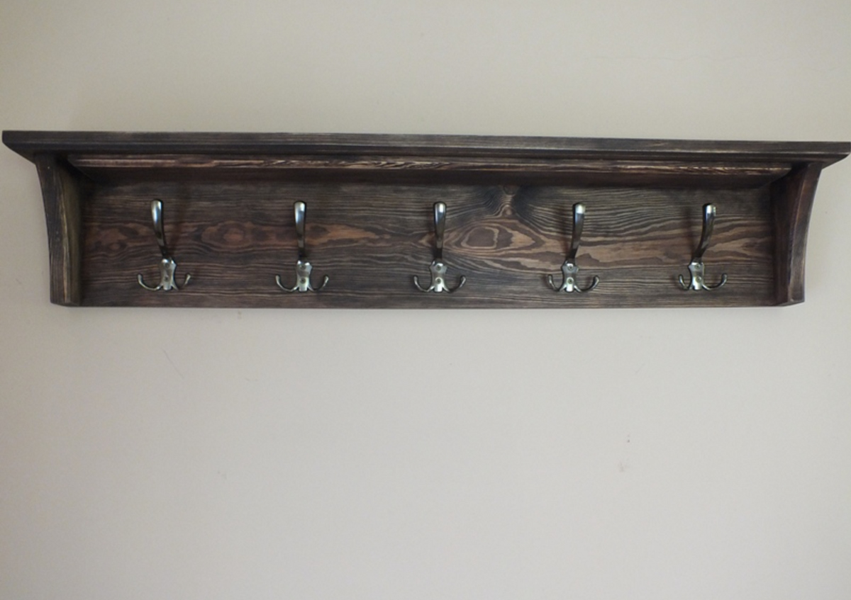 A dark brown wooden wall-mounted coat rack with five silver metal hooks, shown against a plain beige wall.