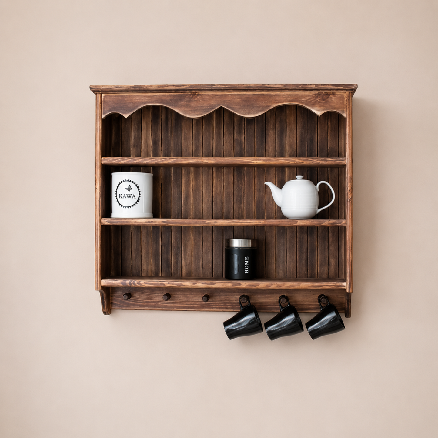 A dark brown wooden wall-mounted shelf with three open tiers and three black hanging mugs below, styled with a white mug, white teapot, and a black canister against a beige wall.