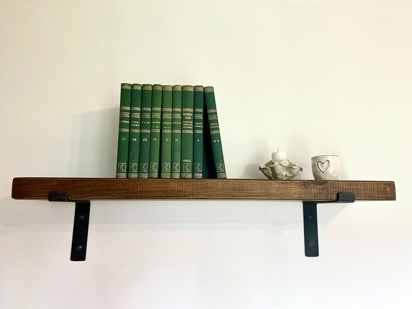 Wooden shelf with green books and decorative items against a white wall