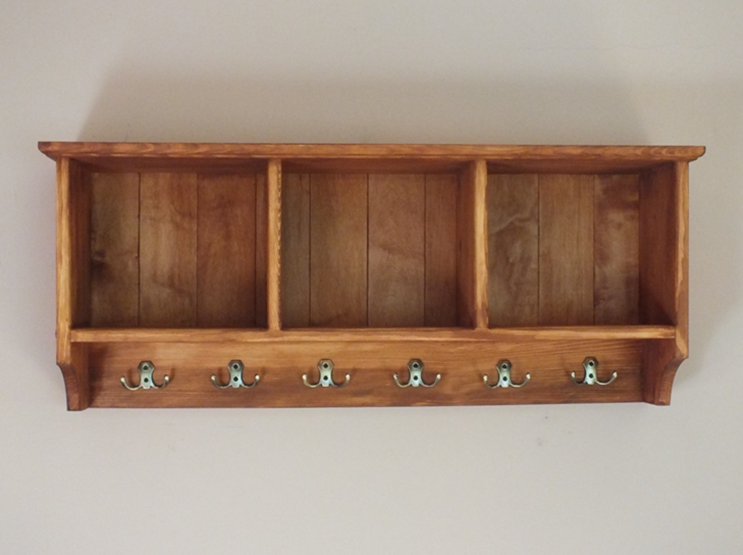 A handcrafted wooden wall-mounted compartments unit with hooks.