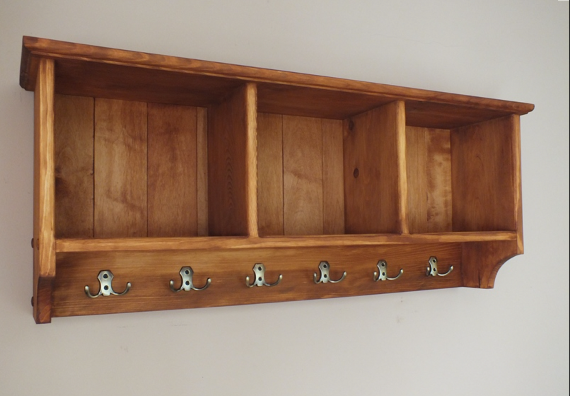A handcrafted wooden wall-mounted compartments unit with hooks.