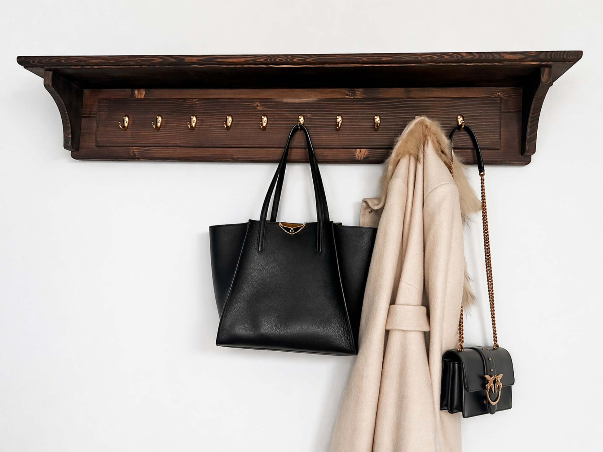 Wooden wall shelf with hooks holding a black handbag, beige coat, and small black bag on a white background.