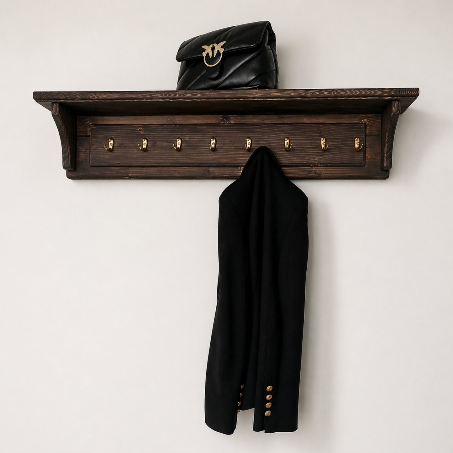 Wooden wall shelf with coat hooks holding a black coat and black handbag on a white background