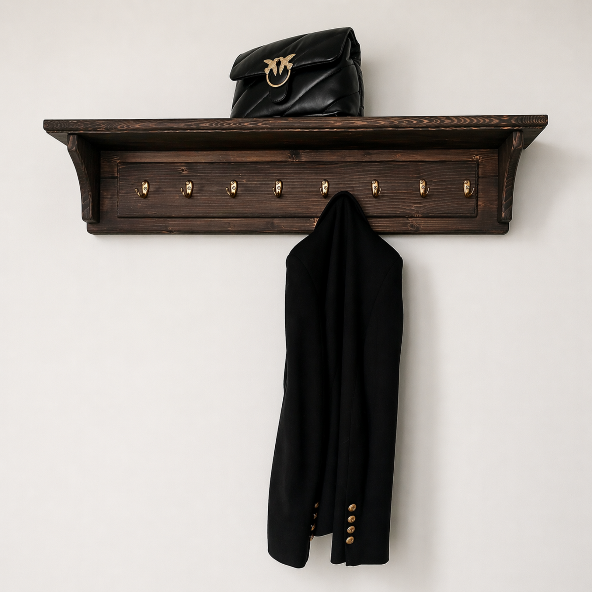 Wooden wall shelf with coat hooks holding a black coat and black handbag on a white background