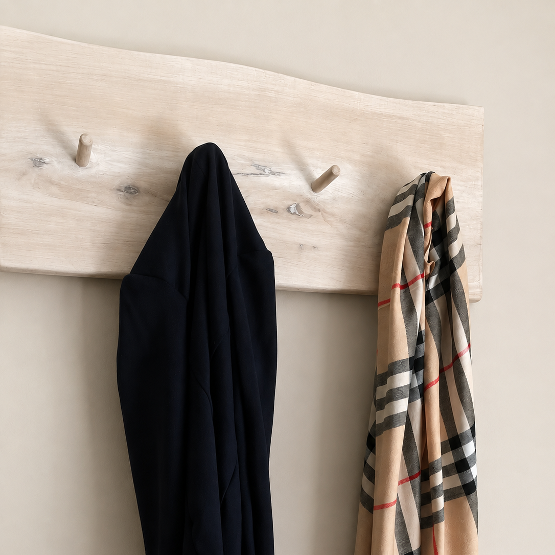 A beige plaid scarf with red and black stripes hangs on a light wood peg rack against a neutral beige wall, next to a dark navy garment.