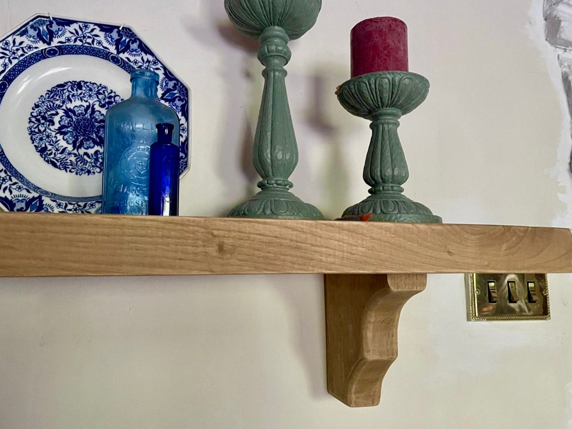 Wooden shelf with decorative items including a blue and white plate, blue bottle, and green candle holders.