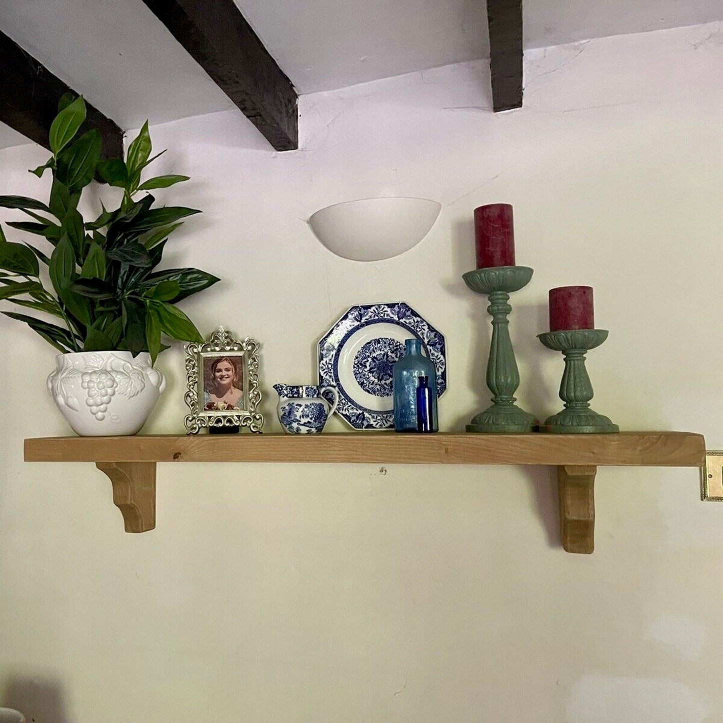 Decorative shelf with a plant, candles, and decorative items against a white wall.