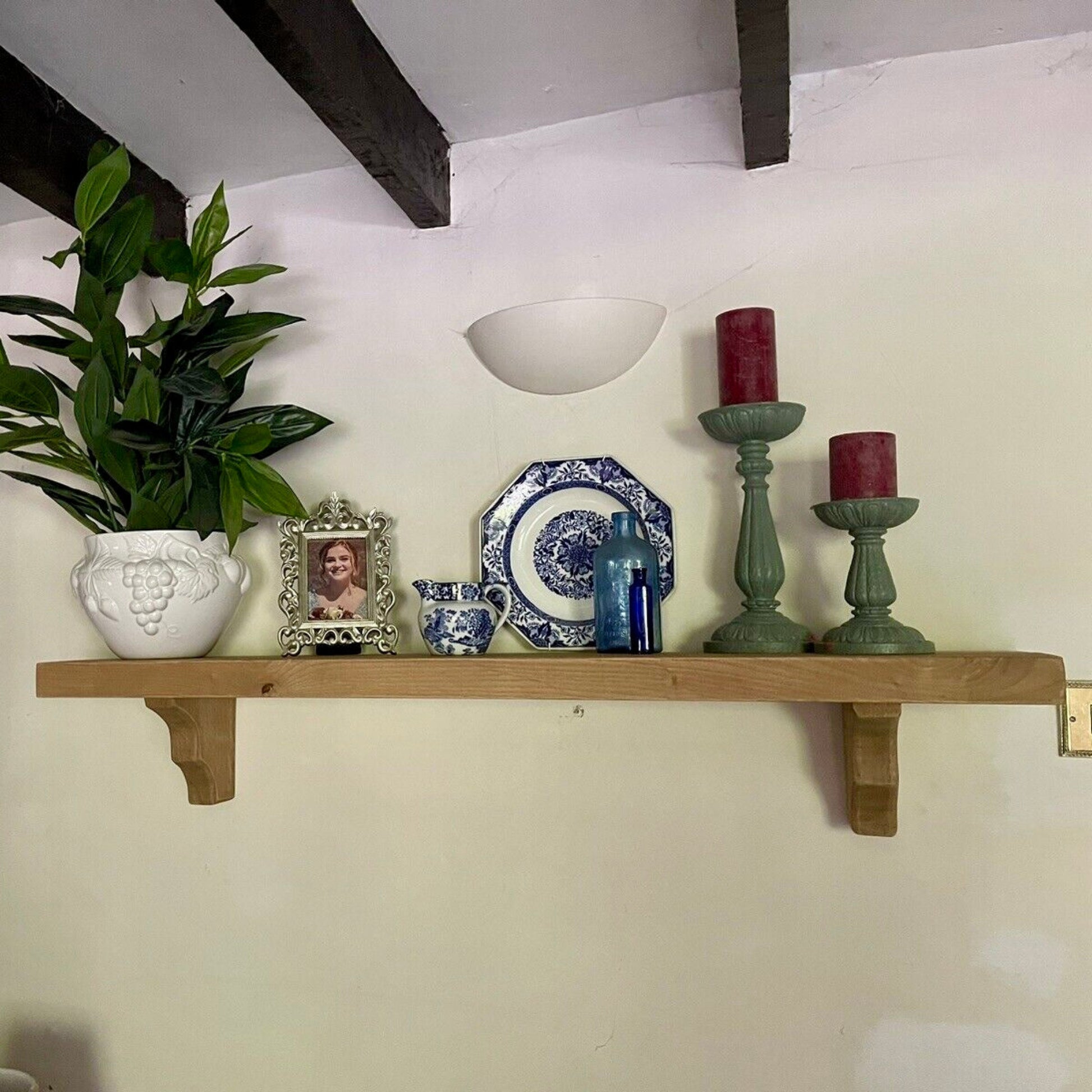 Decorative shelf with a plant, candles, and decorative items against a white wall.