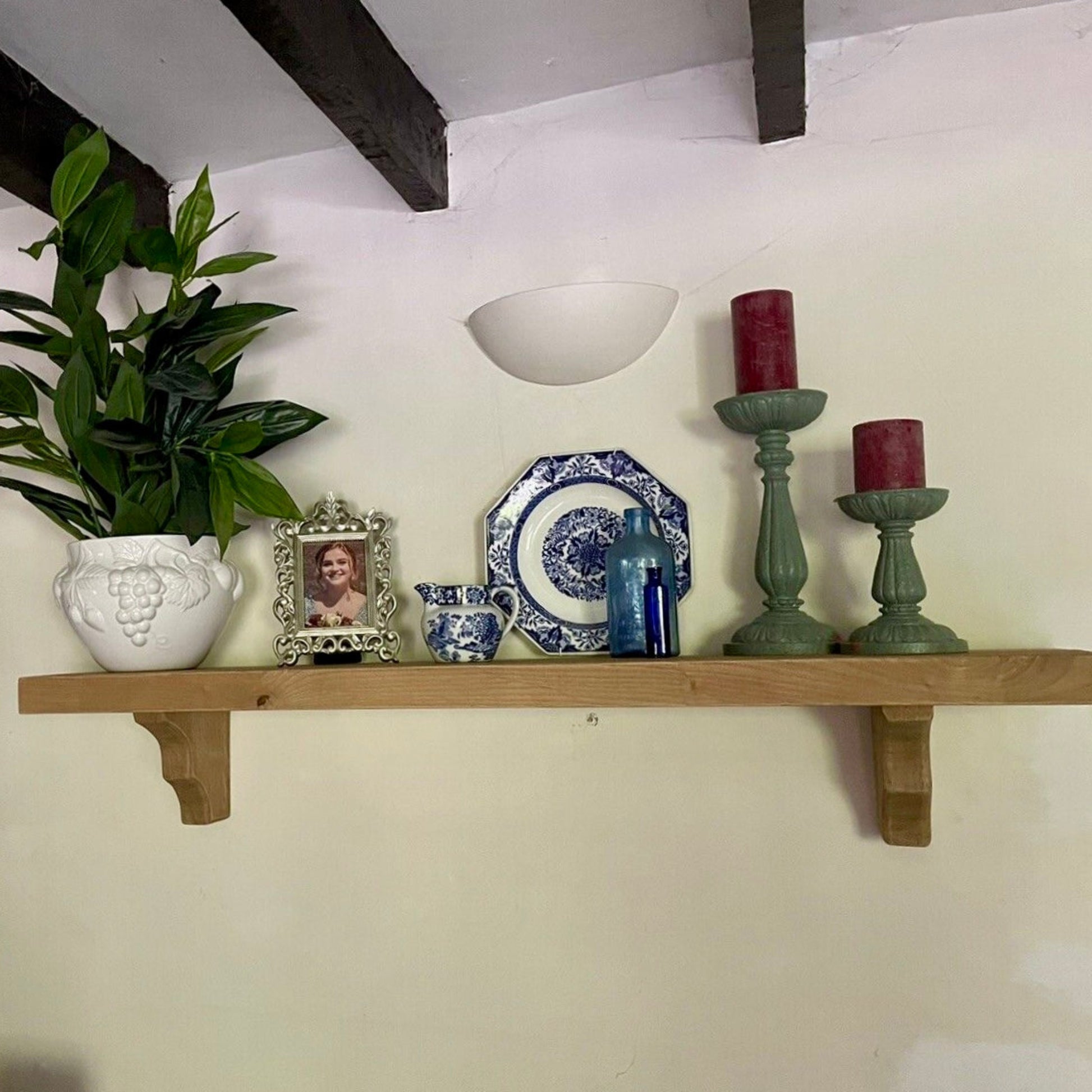 Wooden shelf with decorative items including a plant, picture frame, plates, and candles.