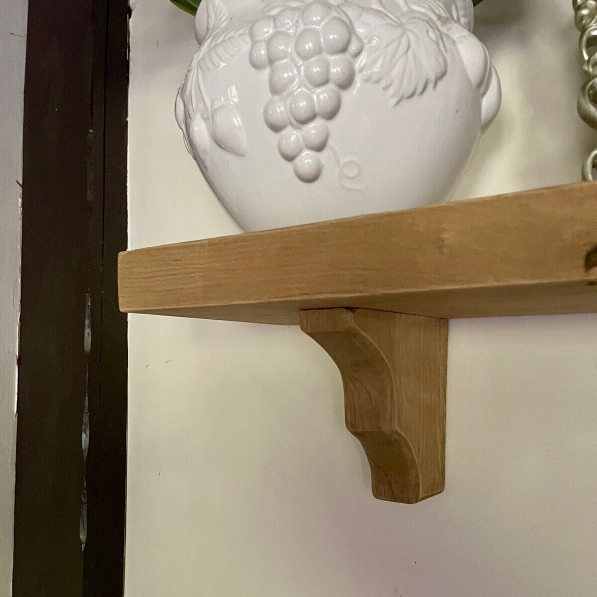 Wooden shelf bracket attached to a white wall with a decorative vase above it.