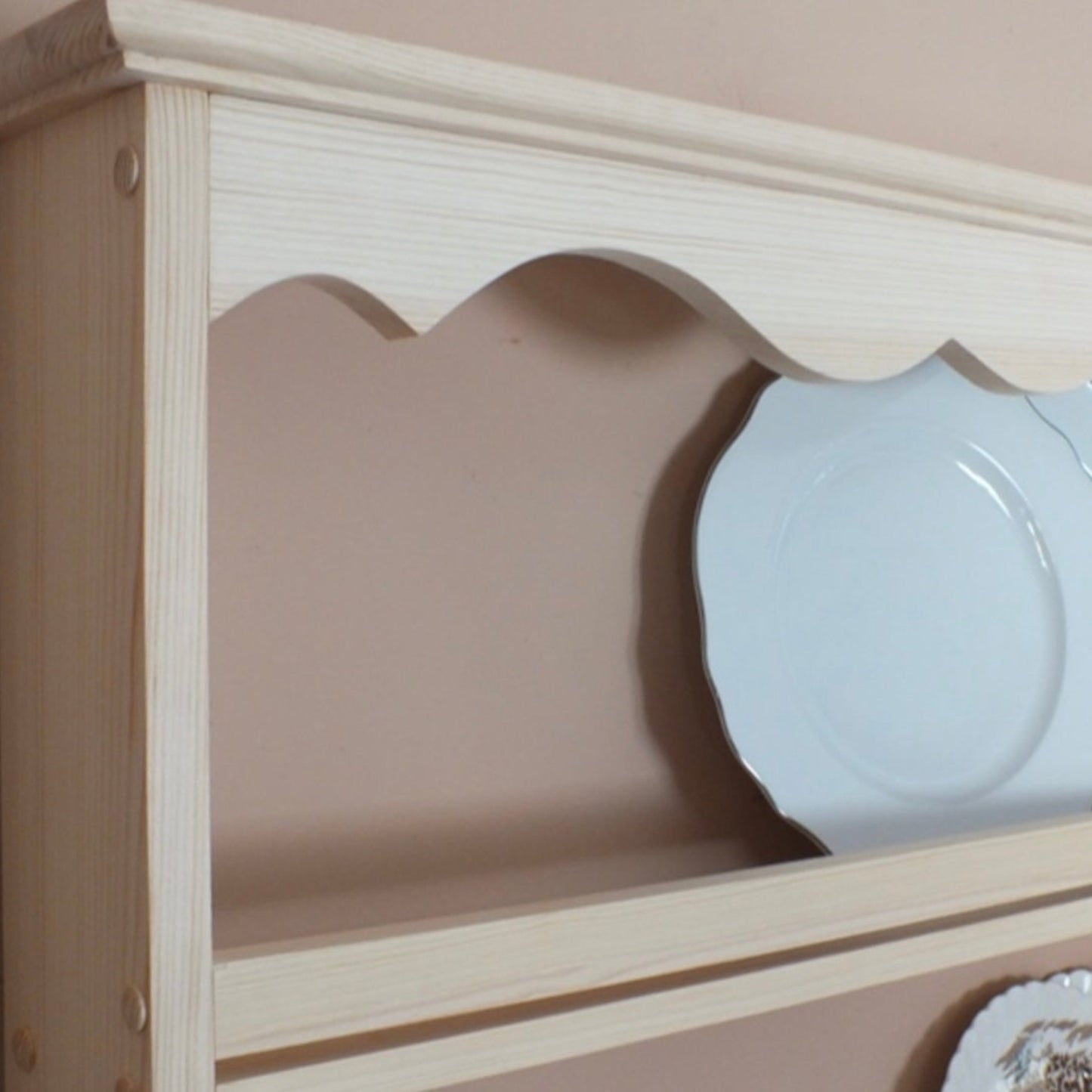 Wooden plate rack with decorative edge holding white plates.