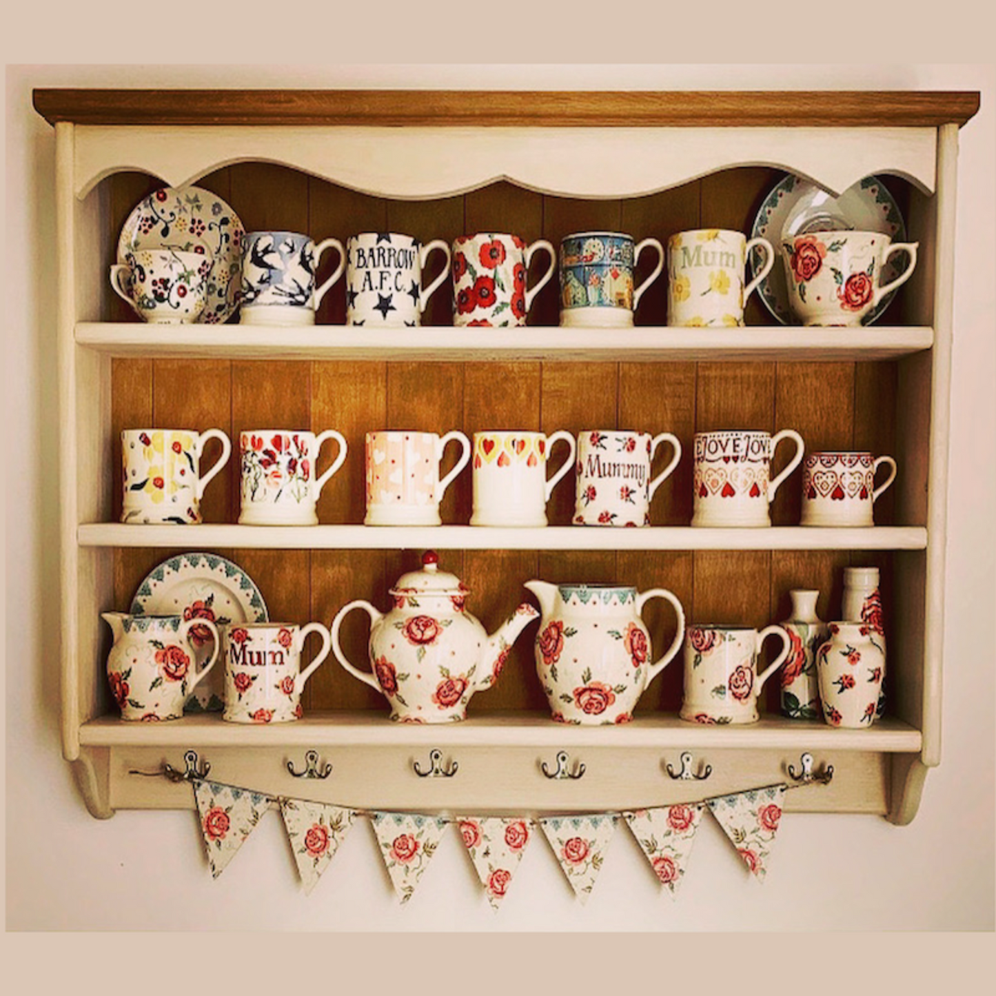 A wooden shelf with a beige finish, wall-mounted, displaying a collection of colorful mugs and decorative items.
