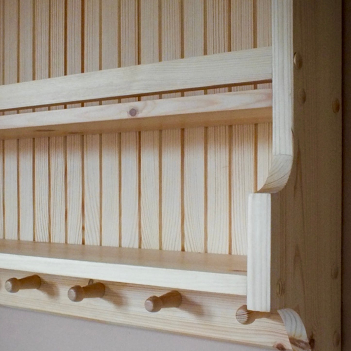 Wooden shelf with horizontal slats and hooks against a wooden wall.