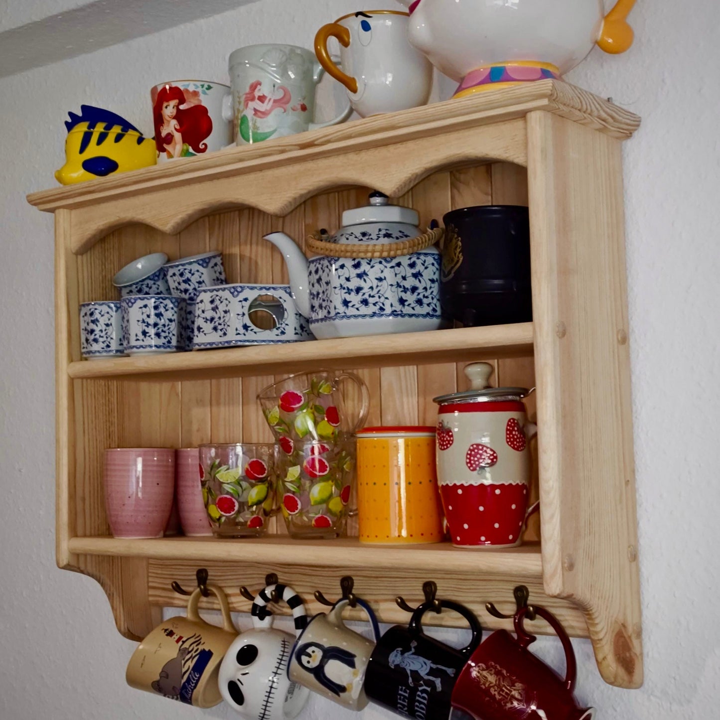 Wooden shelf with decorative mugs, teapots, and a teapot figure on a white wall.