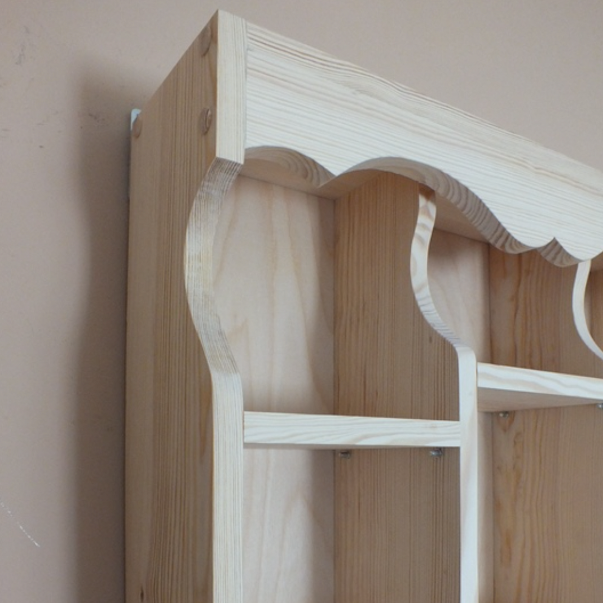Wooden shelf with decorative arches against a plain wall