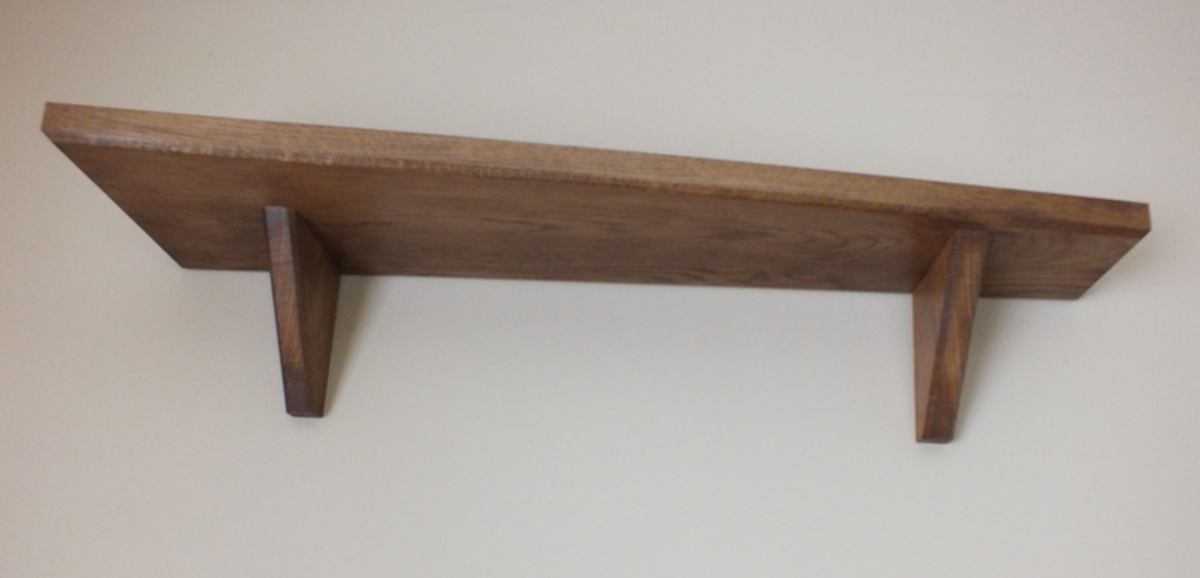 A rustic wooden wall shelf with two angled support brackets, shown against a plain off-white background.