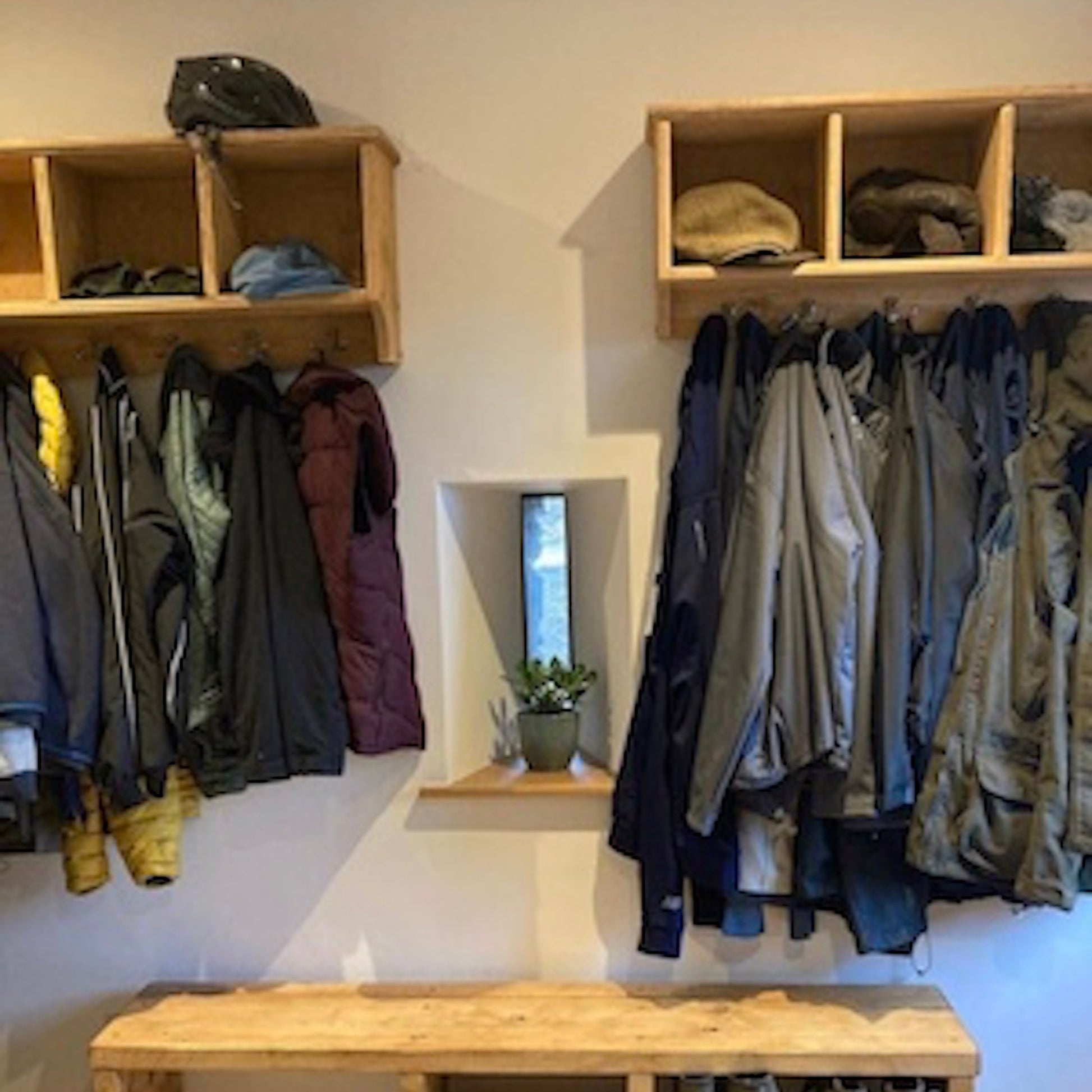 Clothing storage area with wooden shelves and bench, featuring jackets and coats.