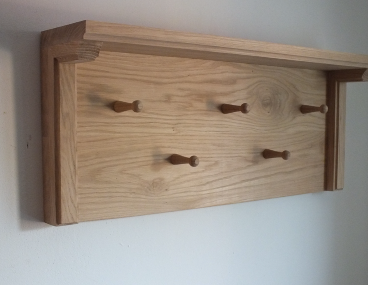 A light natural wood wall-mounted coat rack with five wooden pegs, shown mounted on a plain white wall.