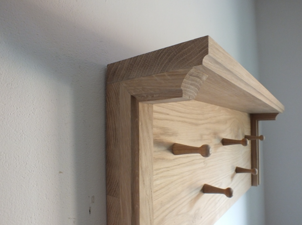 A light oak wood coat rack with four wooden peg hooks, mounted on a textured white wall.