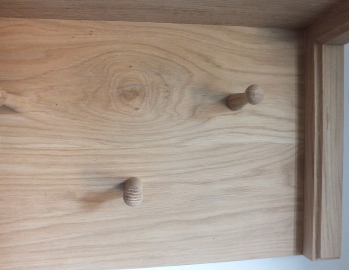 A close-up of a light natural wood wall or cabinet panel with three small round wooden peg hooks attached.