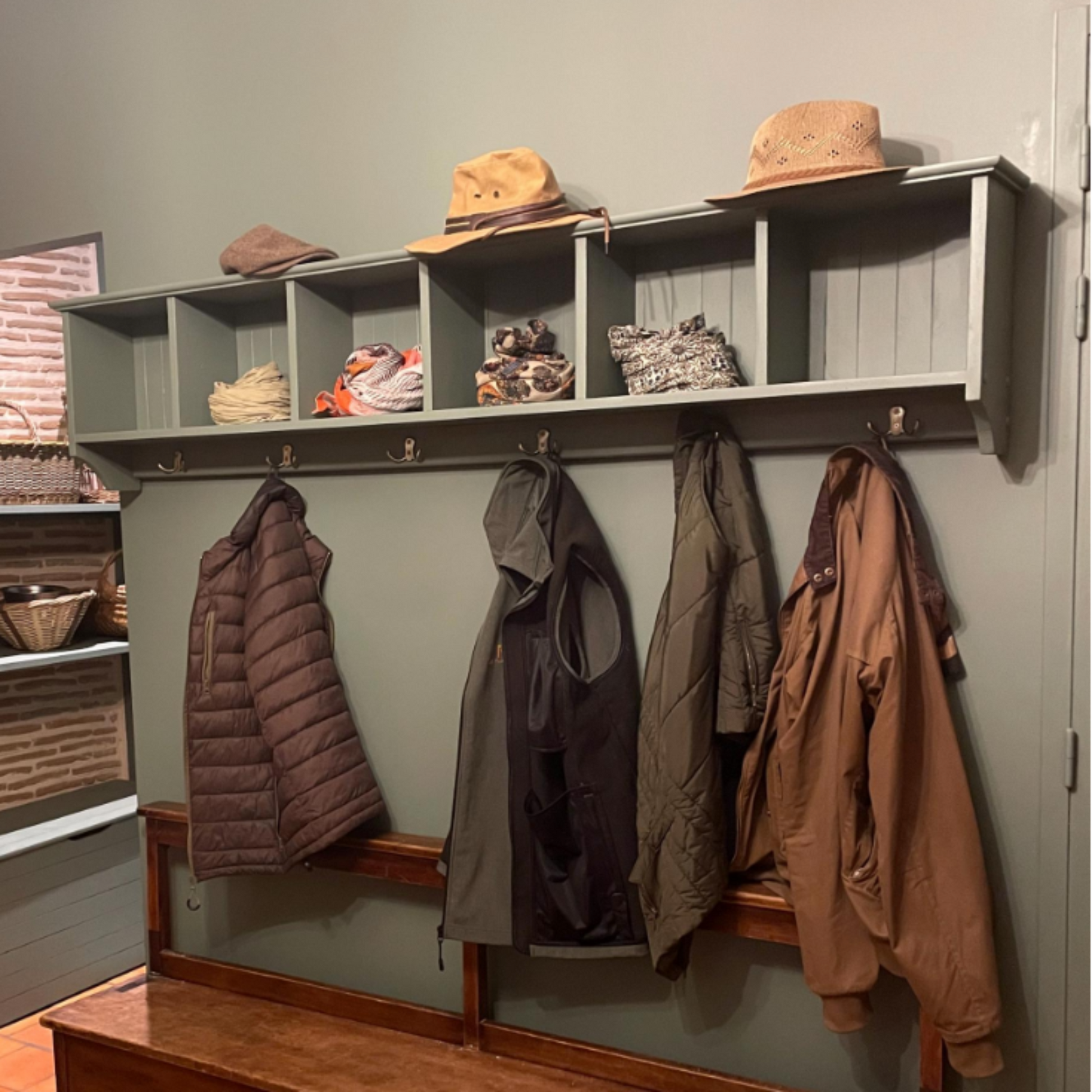 Coat rack with various coats and a wooden bench in a room with green walls and terracotta tiles.