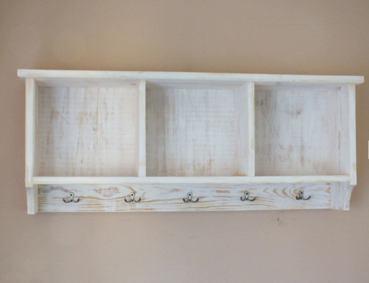 Wooden shelf with four hooks on a plain wall