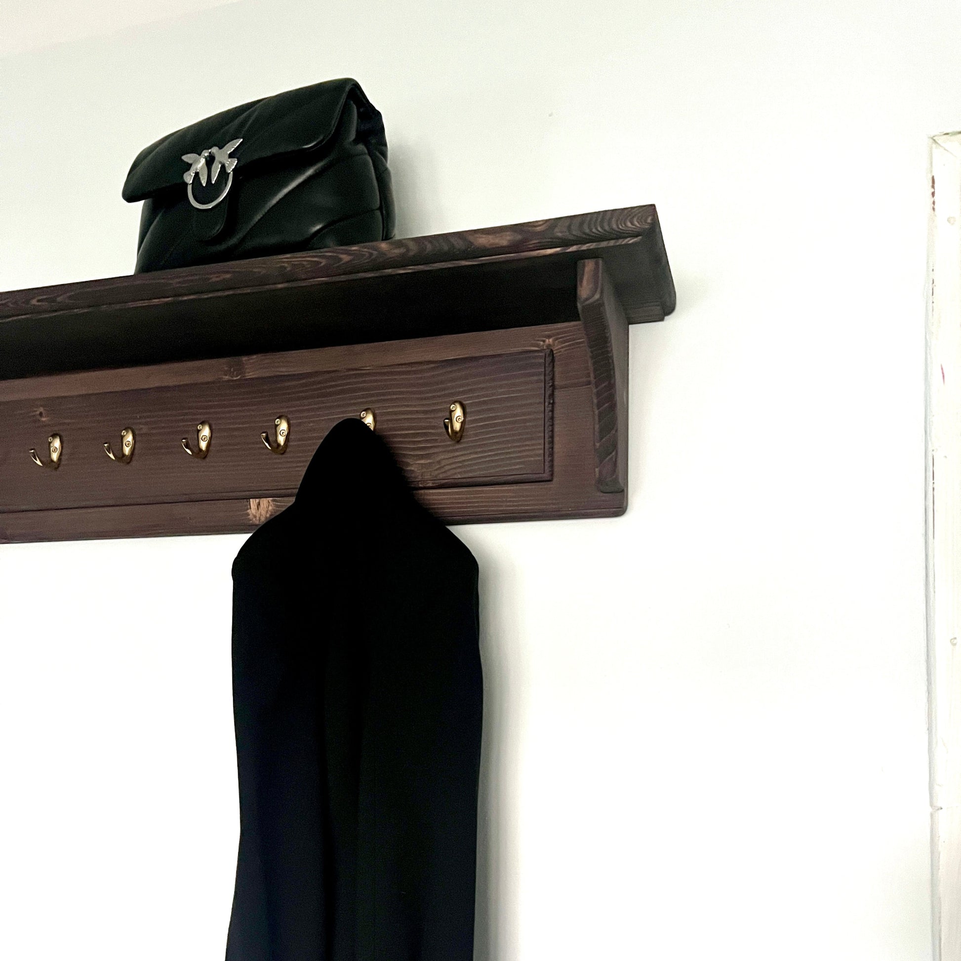 Coat rack with a black coat and bag on a white wall