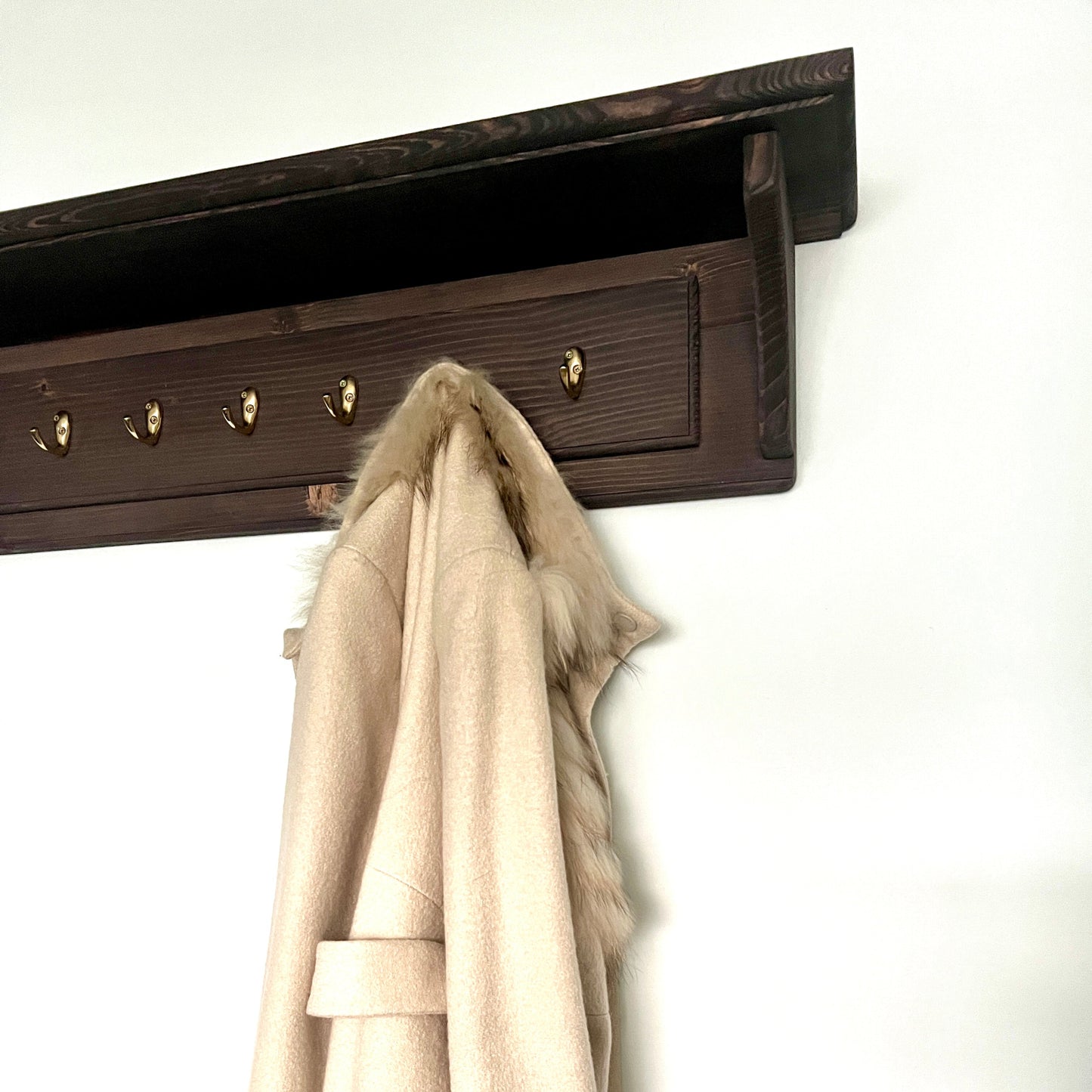 Coat hanging on a wall-mounted coat rack with five hooks.