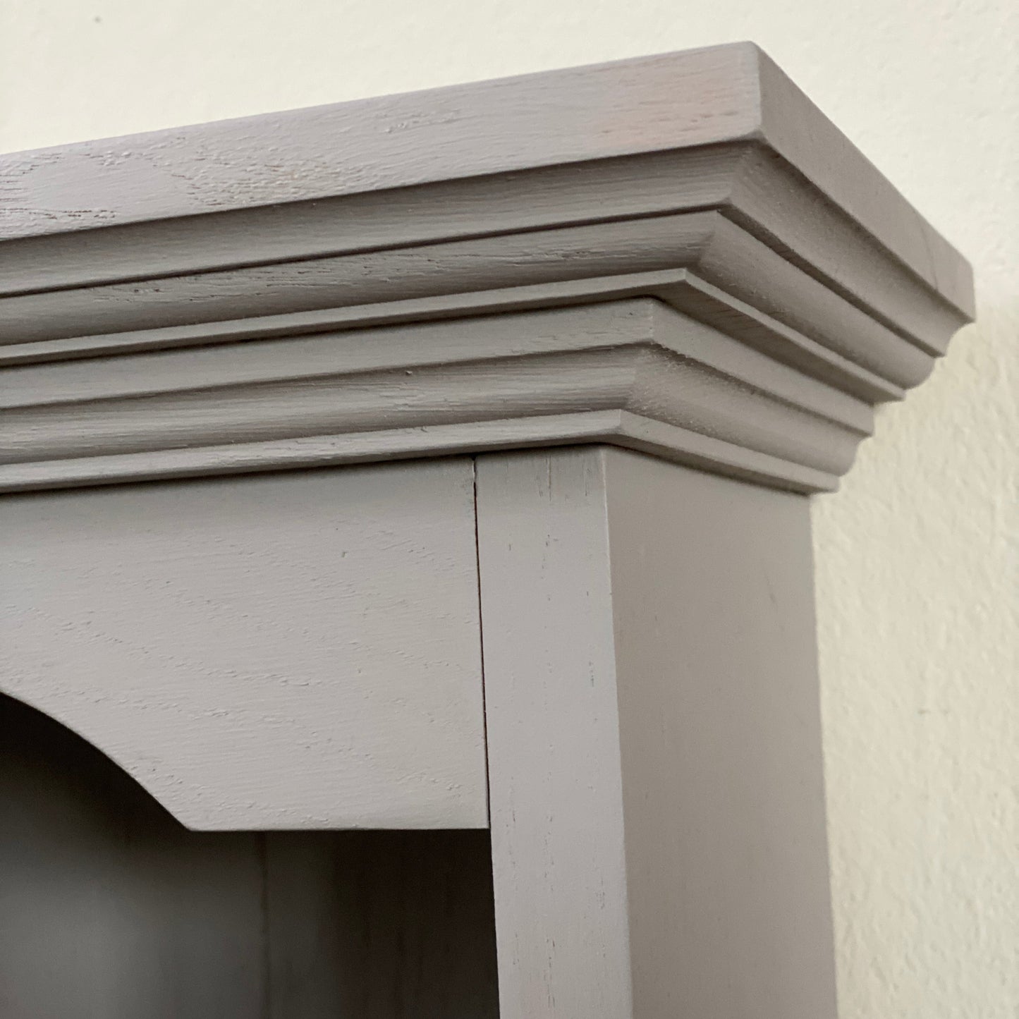 Close-up of a light gray wooden shelf against a white wall.