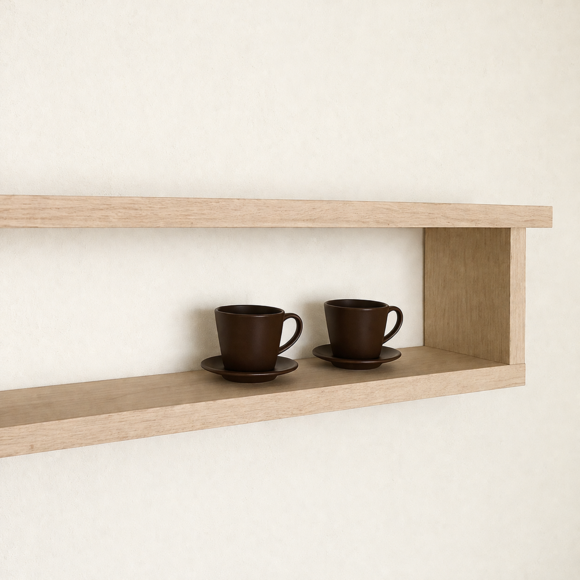 Two brown ceramic cups on saucers on a wooden shelf against a white wall.