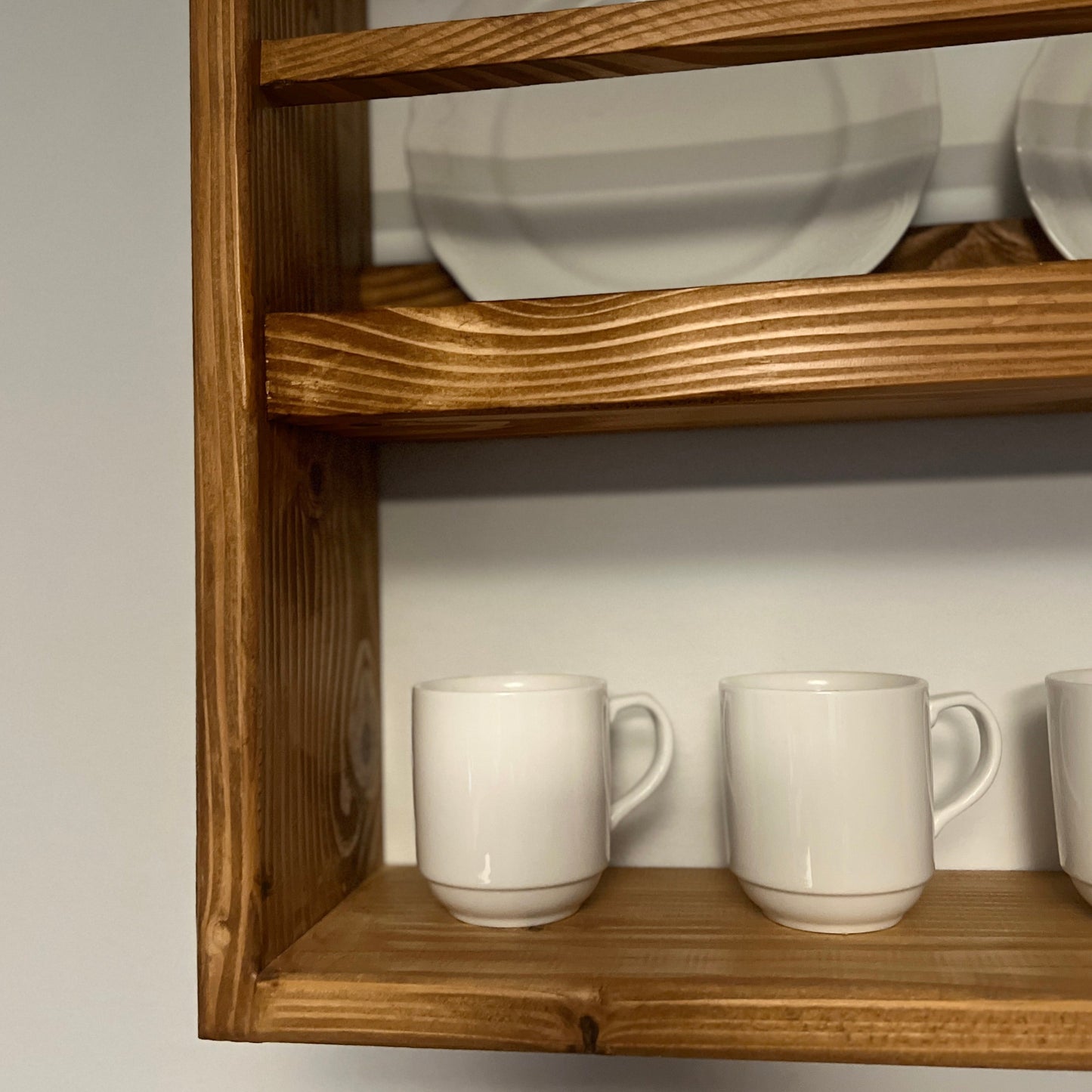 Wooden shelf with white mugs and plates on a plain background