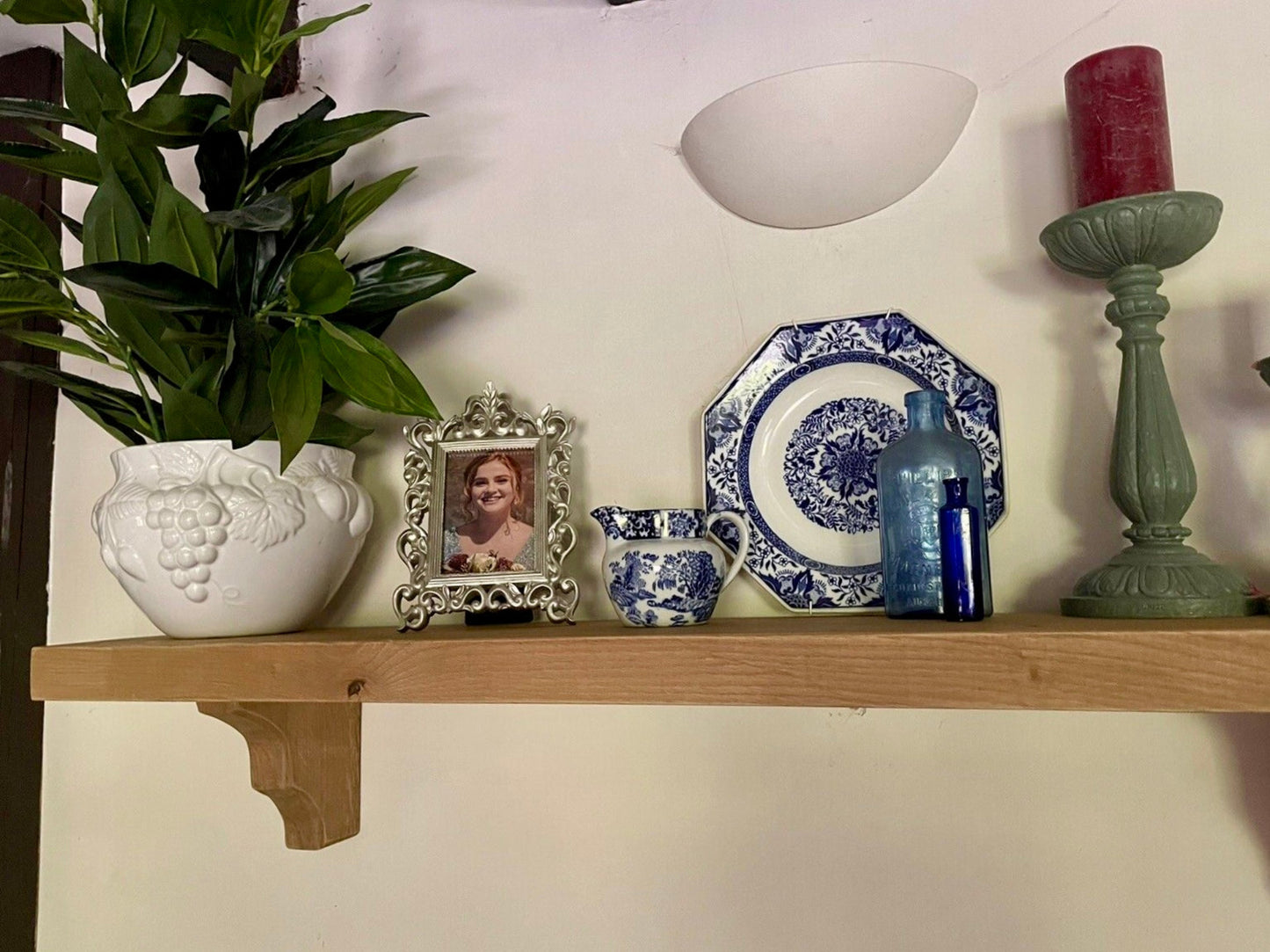 Decorative shelf with a plant, framed photo, teacup, plate, and candle.