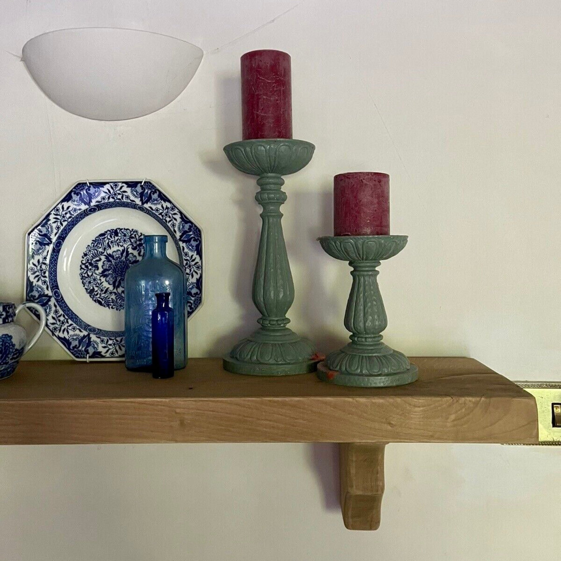 Decorative shelf with candles, plates, and a vase against a white wall.