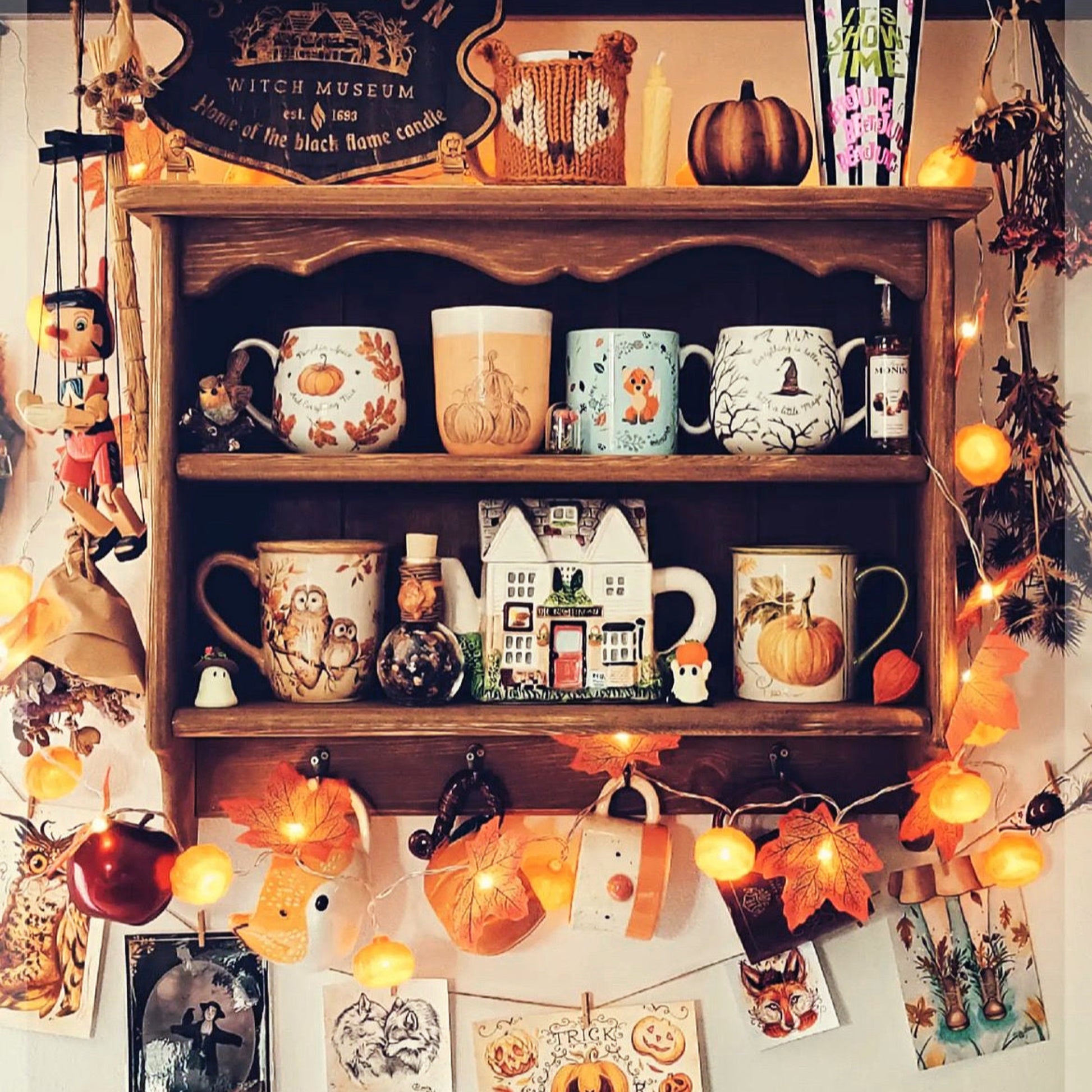Wooden shelf with Halloween-themed mugs and decorations, including pumpkins and string lights.