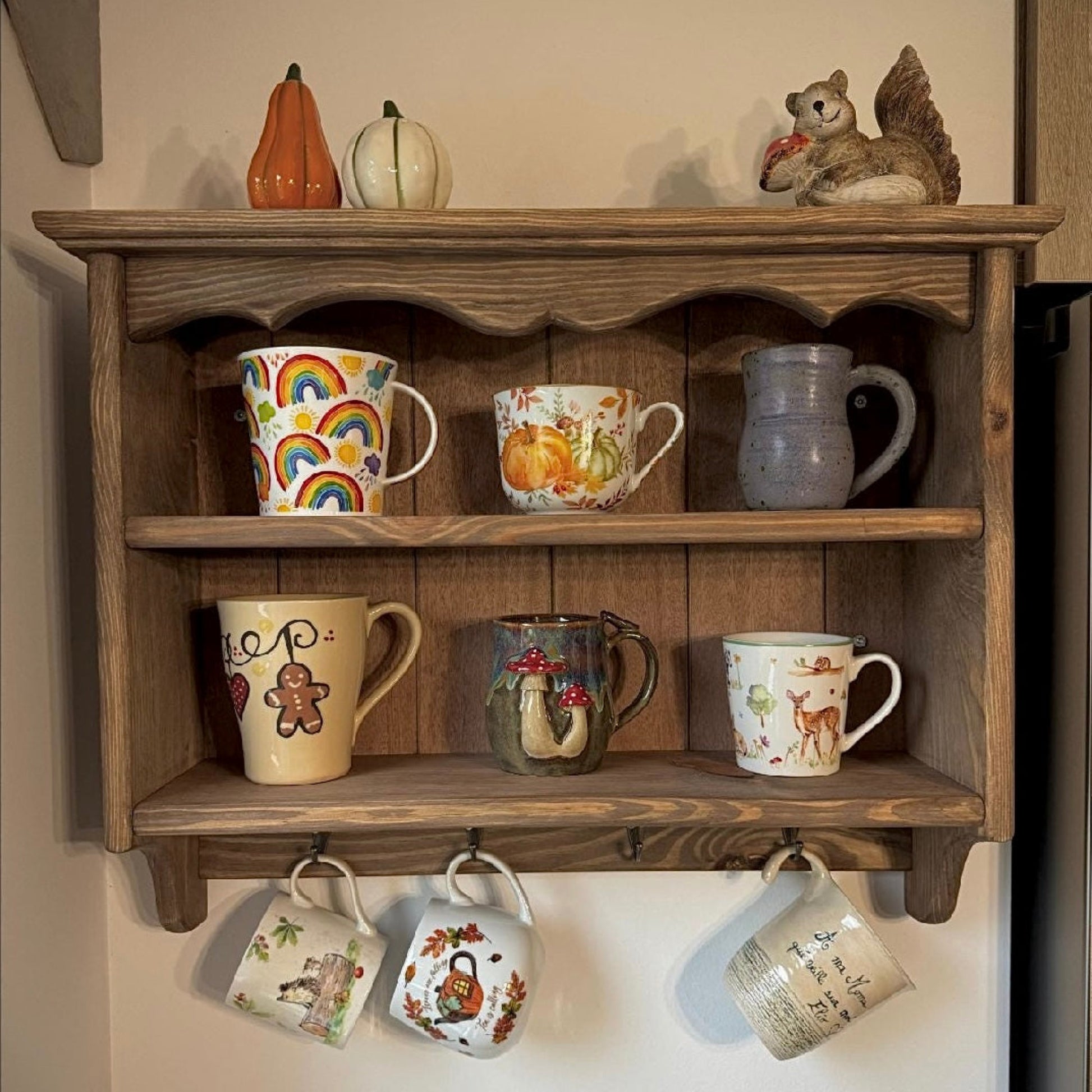 Wooden shelf with decorative mugs and small pumpkins on a wall.