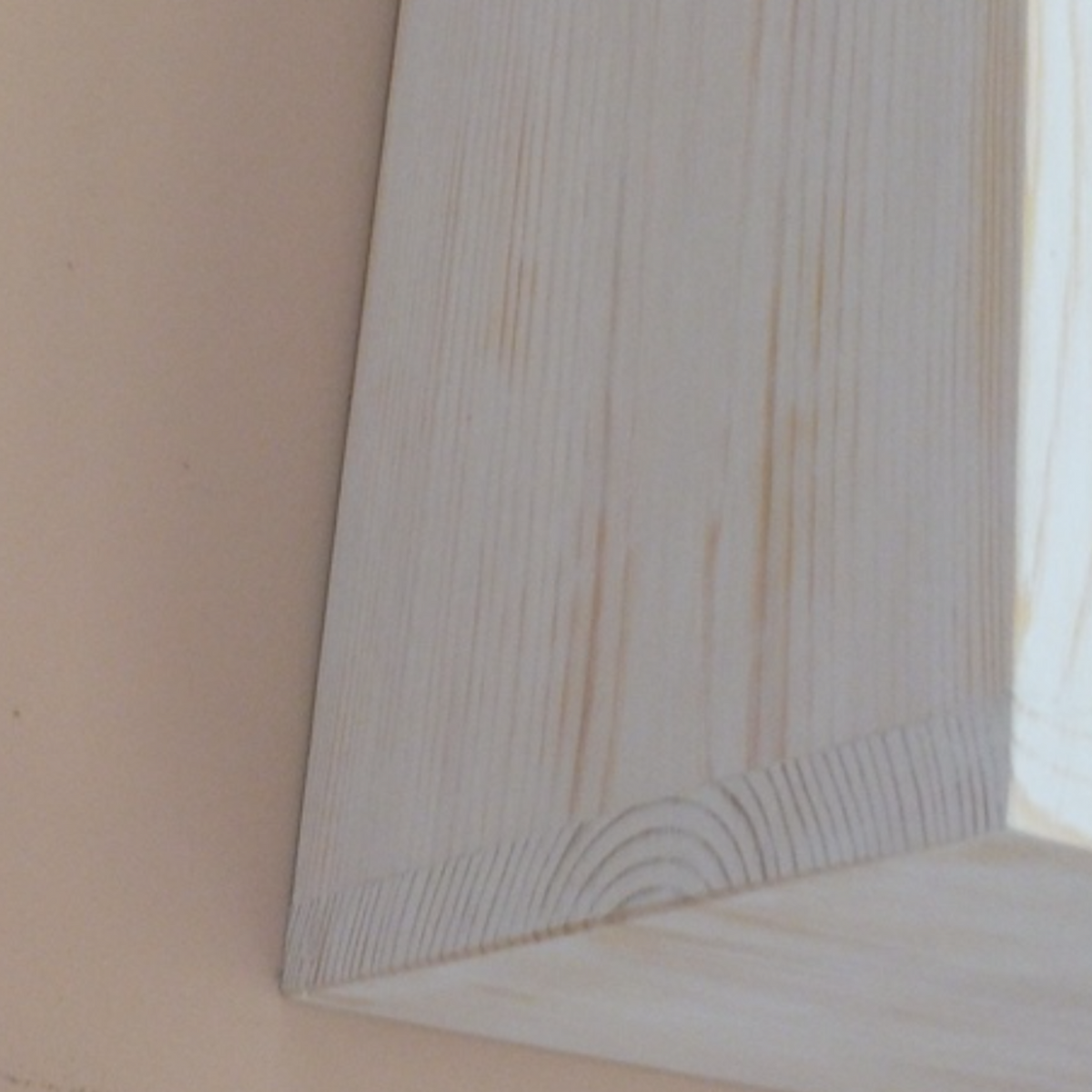 Close-up of a white-painted wooden frame or panel corner against a beige wall.