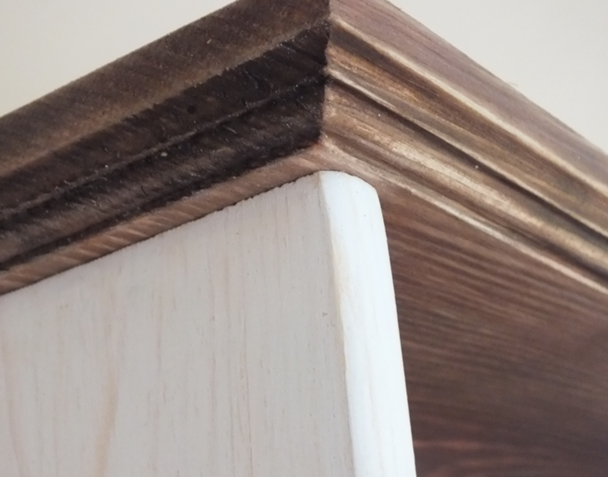 Close-up of a wooden shelf or cabinet corner with a dark brown stained top edge and a white painted side panel.