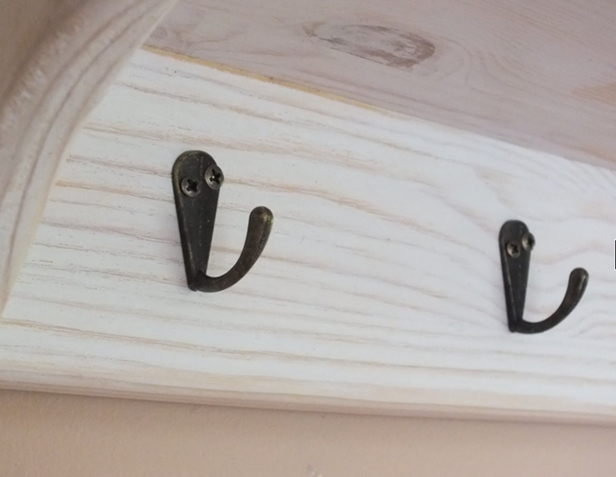 Two dark metal coat hooks mounted on a white-painted wooden board, shown in a close-up interior shot.